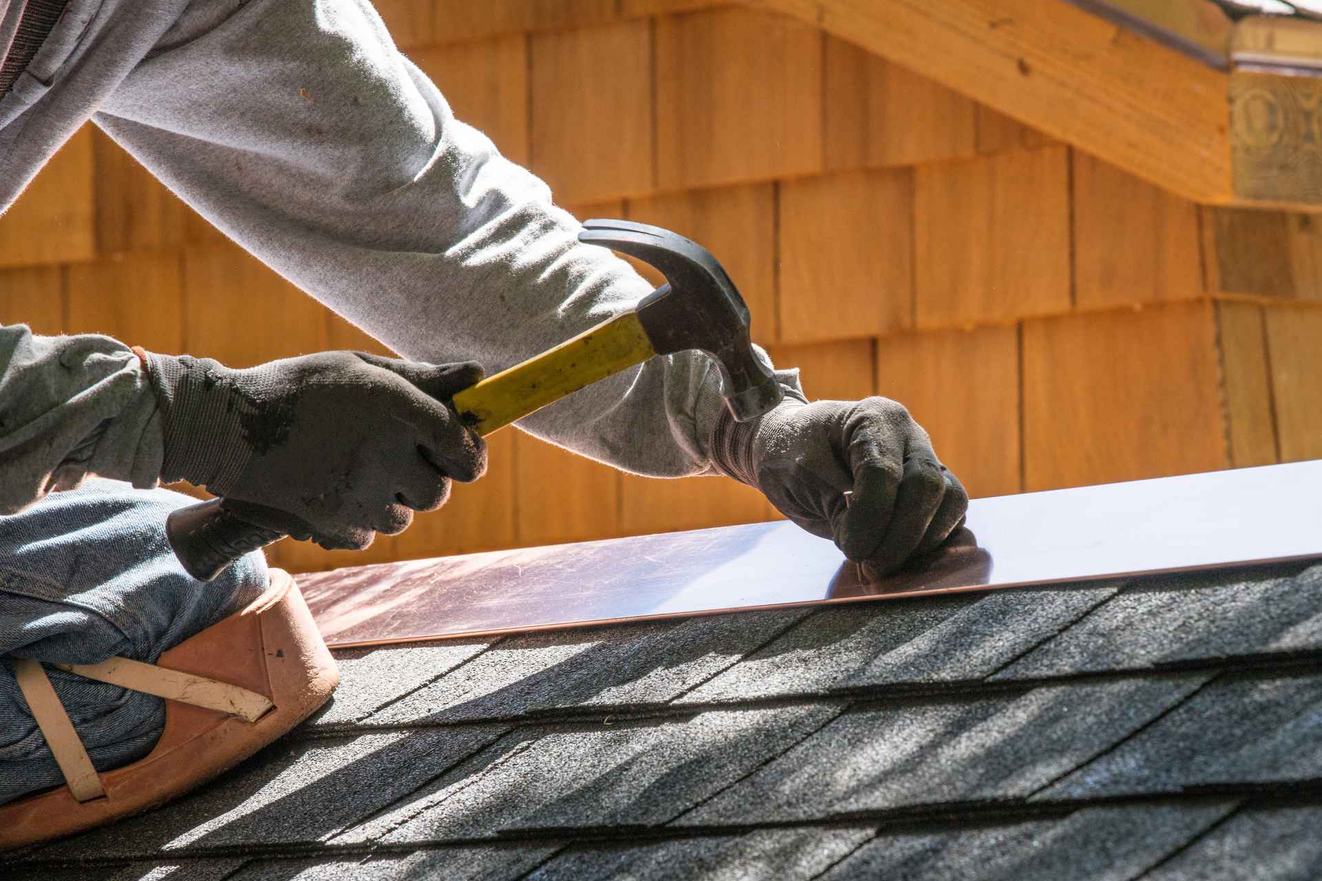 Close-up of a professional installer securing metal roof flashing along a residential roof seam.